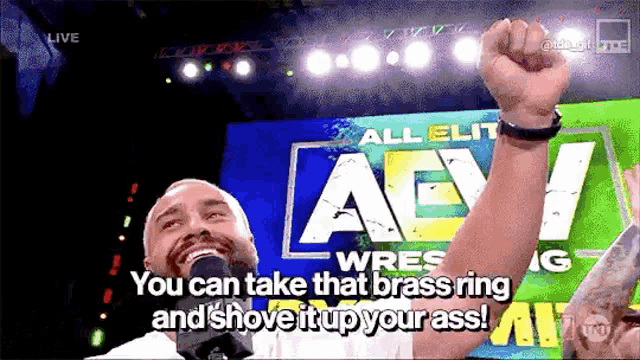 a man is holding his fist up in the air in front of a sign that says all elite wrestling .