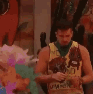 a man wearing a yellow tank top with a cartoon character on it is looking at his phone .