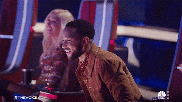 a man is laughing while sitting in front of a nbc sign