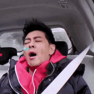 a man wearing a red hoodie is yawning in a car