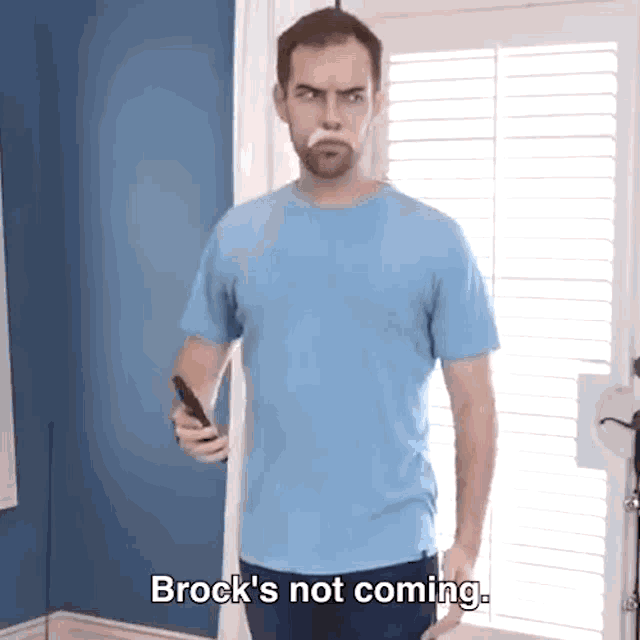 a man in a blue shirt is holding a remote control and says brock 's not coming