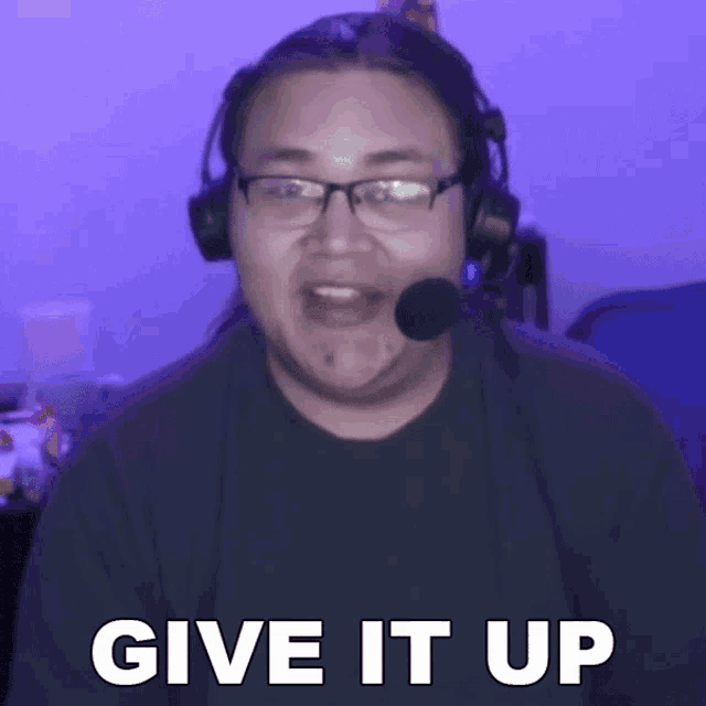 a man wearing headphones and a microphone is saying give it up