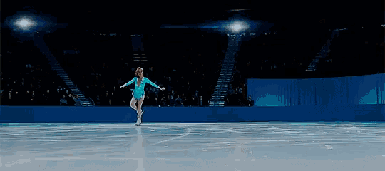 a woman in a blue dress is ice skating in front of a crowd
