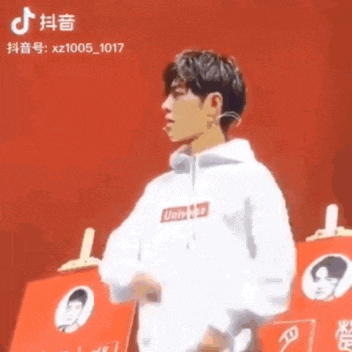 a man in a supreme hoodie is standing in front of a red wall .