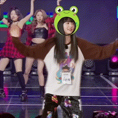 a girl wearing a frog hat is dancing on a stage with her arms outstretched