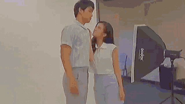 a man and a woman are standing next to each other in a room in front of a camera .