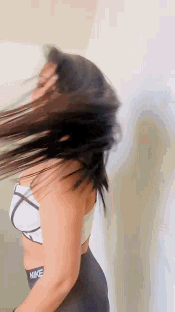 a woman wearing a nike bra and leggings is spinning her hair