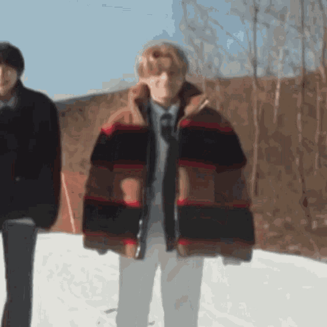 a man and woman are walking in the snow and the woman is wearing a striped jacket