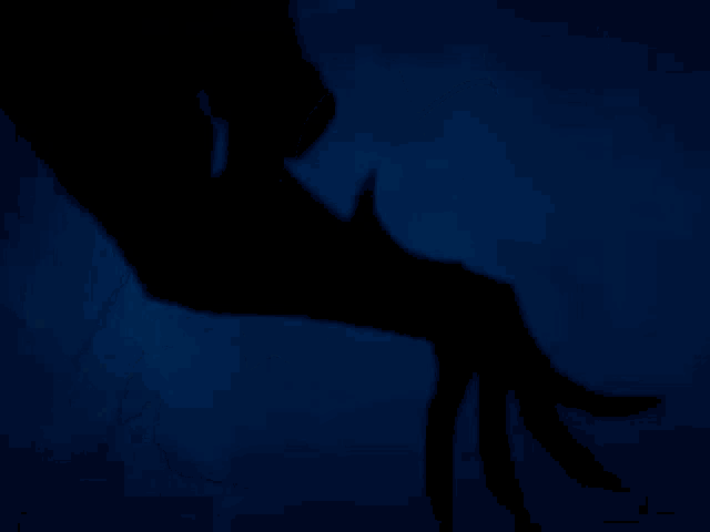 a silhouette of a batman with a light on his face against a dark blue background .