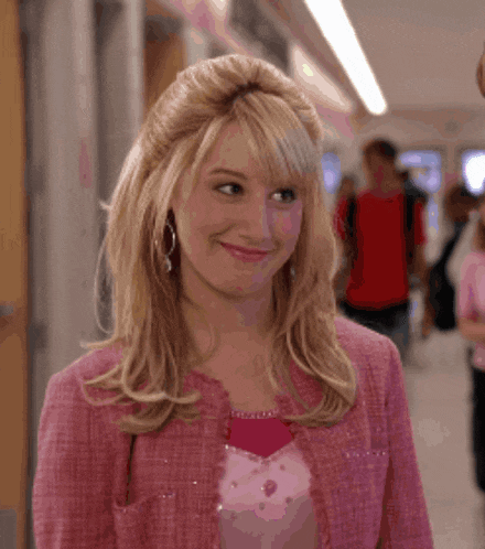 a blonde woman wearing a pink jacket and pink shirt smiles