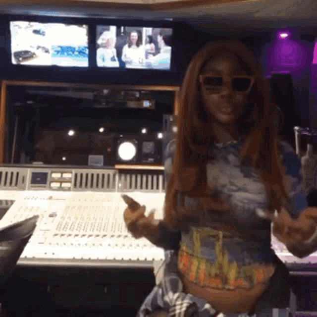 a woman wearing sunglasses stands in front of a mixer in a recording studio