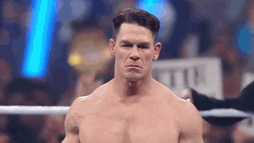 a shirtless wrestler is standing in a boxing ring and making a face .