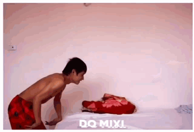 a shirtless man standing next to a bed with a blanket on it .