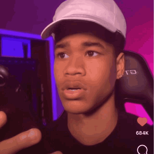 a young man wearing a white hat is making a funny face while sitting in a chair .
