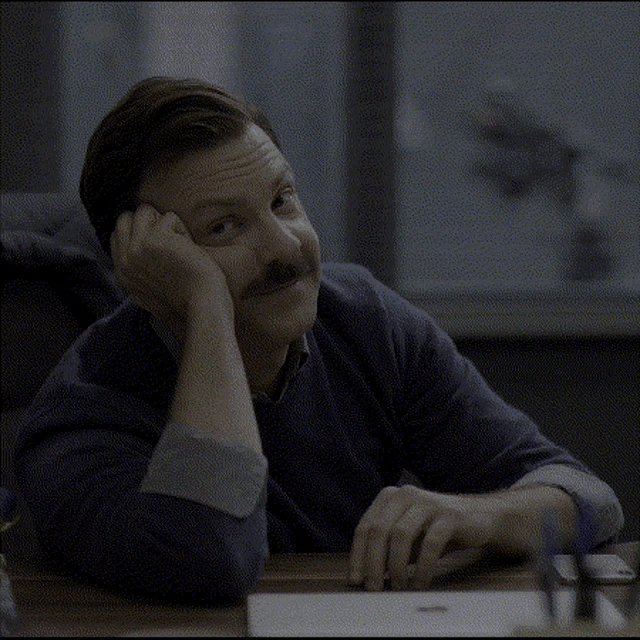 a man is sitting at a desk with his head resting on his hand .