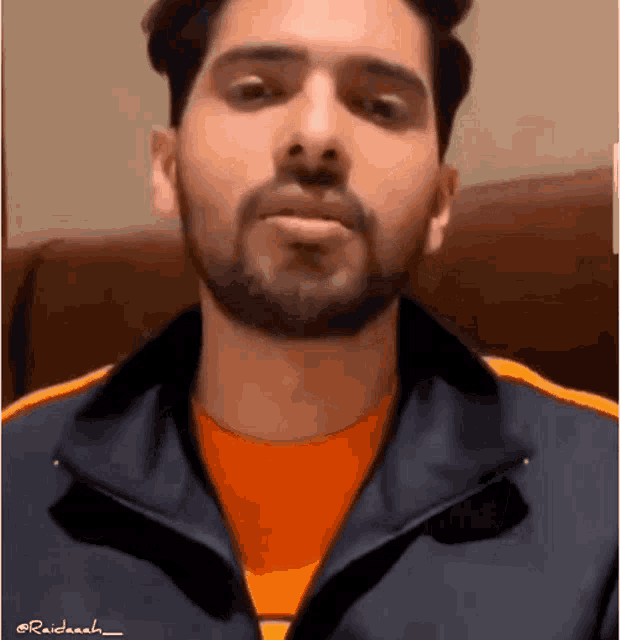 a man with a beard is wearing a blue jacket and an orange shirt .