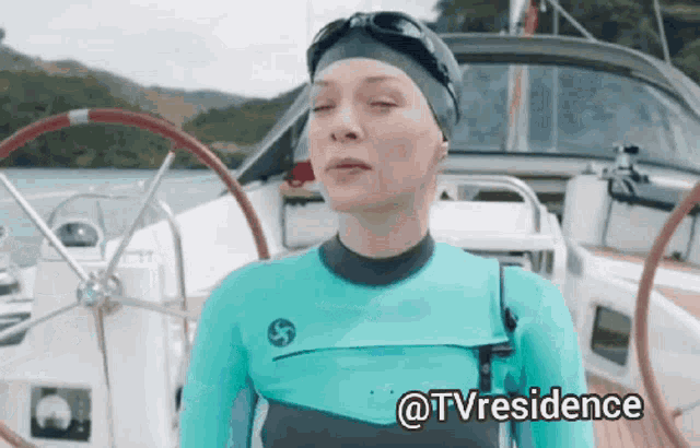 a woman in a wet suit is standing on a boat with the words @tvresidence written below her