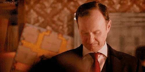 a man in a suit and tie is looking down with a bbc one logo in the background .
