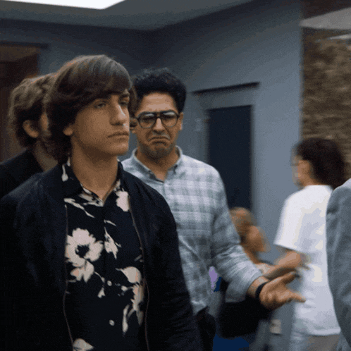 a man wearing glasses and a floral shirt stands in a crowd of people