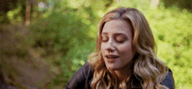 a woman is sitting in the woods with her eyes closed and a smile on her face .