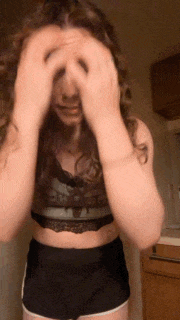 a woman in a crop top and shorts covering her eyes with her hands