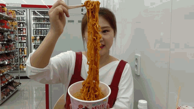 a woman in a red apron is eating noodles with chopsticks