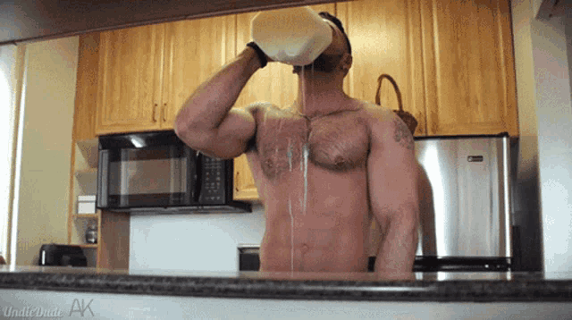 a shirtless man drinking milk from a pitcher in a kitchen with the words indiewhite ak on the counter