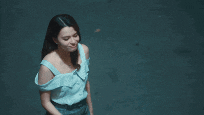 a woman in a blue off the shoulder top stands in front of a dark wall