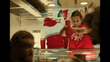 a woman in a red shirt that says ' siga ' on it is pouring ketchup