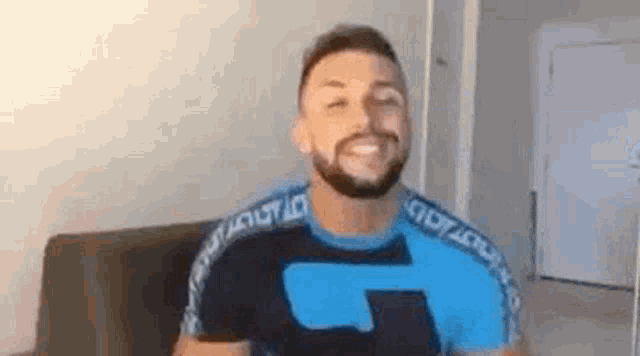 a man with a beard is sitting on a couch wearing a blue shirt .