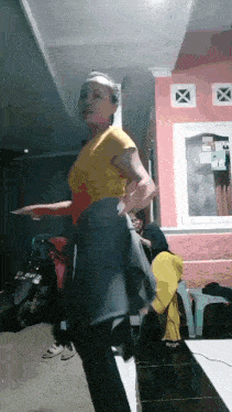 a woman in a yellow shirt is dancing in a room with a motorcycle parked behind her