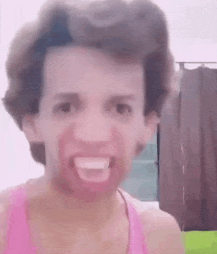 a man wearing a pink tank top is making a funny face with his mouth open .