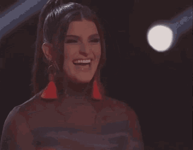 a woman with a ponytail and red tassel earrings is laughing