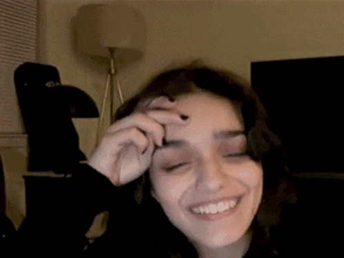 a woman is smiling and touching her forehead while sitting in a living room .