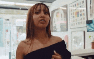 a woman in a black off the shoulder top is standing in a room with paintings on the walls .