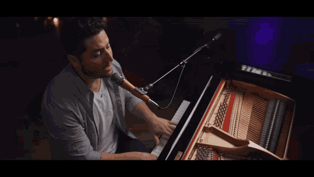 a man sitting at a piano singing into a microphone