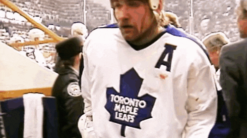 a hockey player wearing a white jersey with a maple leaf on it is walking on the ice .