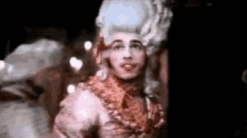 a man wearing a wig and a dress is standing in a room .