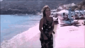 a woman in a black dress is standing on a beach near the ocean .