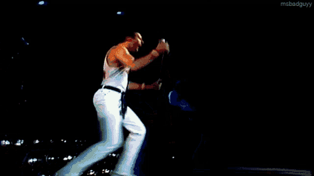 a man in white pants is singing into a microphone while dancing on a stage .