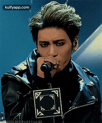 a young man in a leather jacket is singing into a microphone .