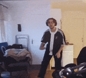 a man wearing headphones and a black adidas shirt is dancing in a living room .