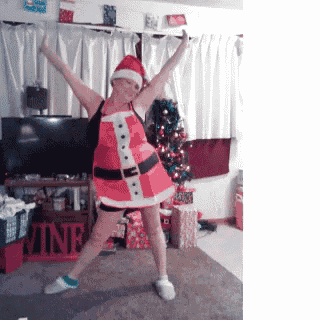 a woman in a santa costume stands in front of a christmas tree