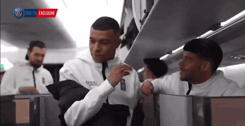 a man in a qatar airlines jacket talks to another man on a plane