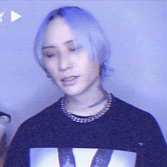 a young man with purple hair is wearing a black sweater and a necklace .