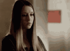 a woman with long hair is standing in front of a wall and looking down .