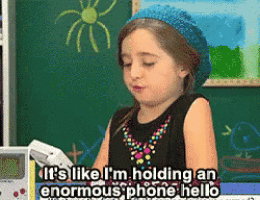 a little girl is holding a cell phone and saying it 's like i 'm holding an enormous phone