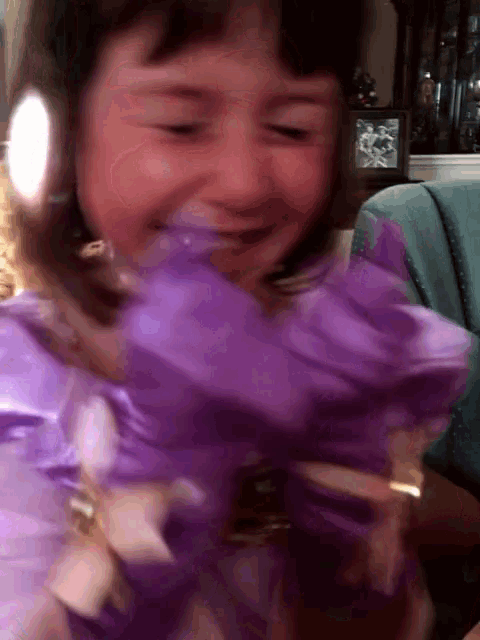a little girl in a purple dress is smiling while holding a purple flower