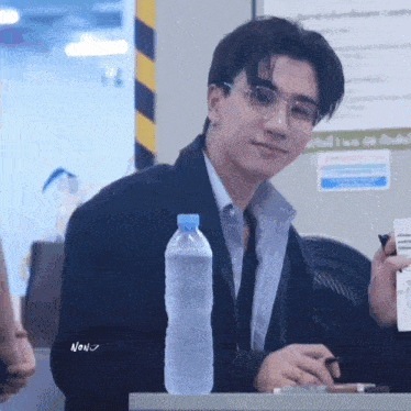 a man wearing glasses is sitting at a table with a bottle of water in front of him