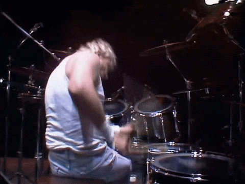 a man in a white tank top is playing drums in a dark room